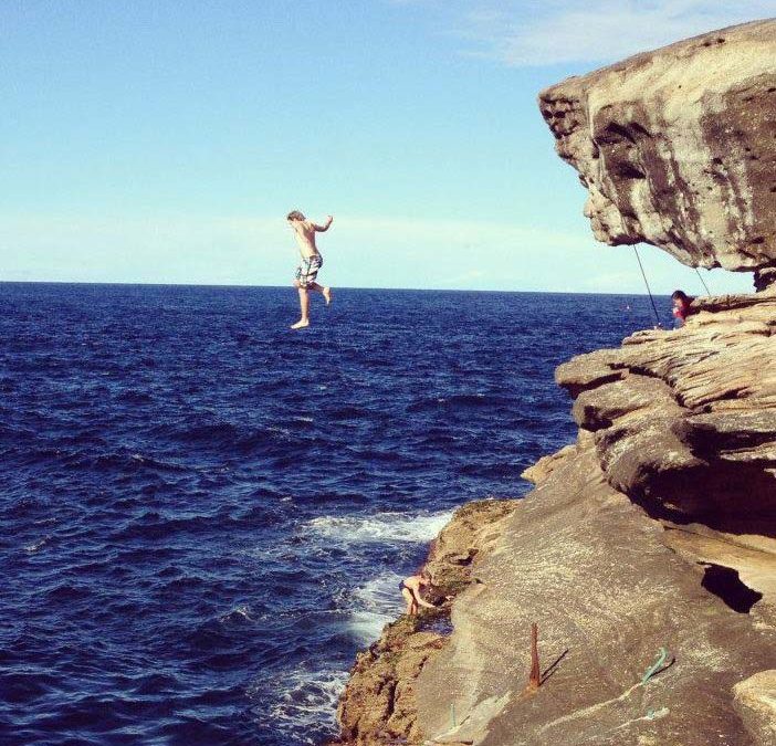 A young male jumping off a cliff into the ocean